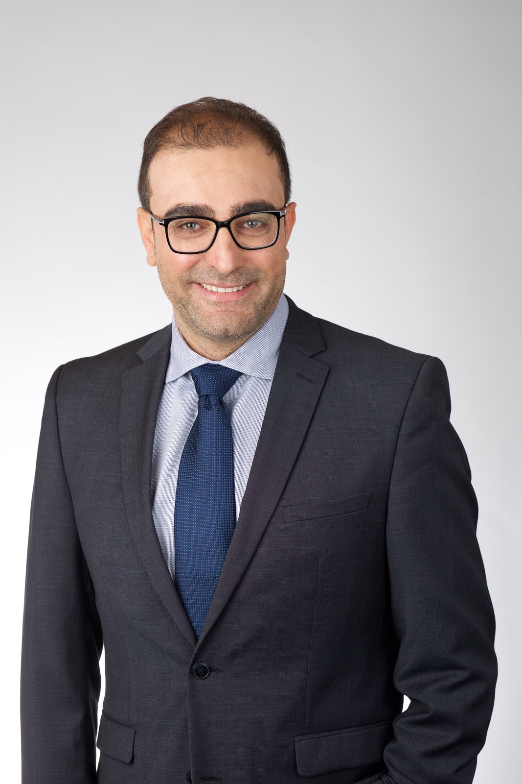 Fellowship application headshot — man with glasses in a charcoal suit and blue tie, New York